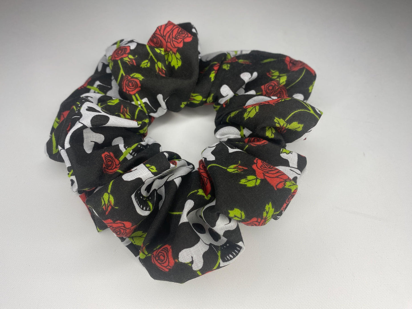 A studio style photo of a large sized scrunchie with skull and crossbones and red roses.