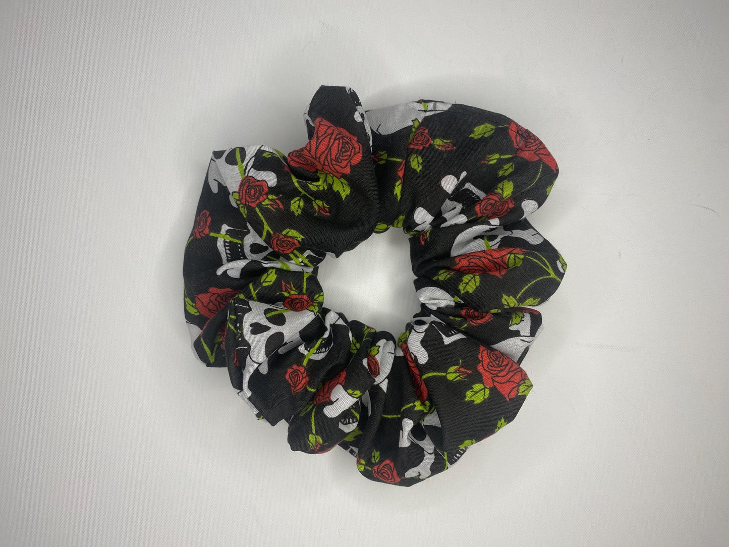 A studio style photo of a large sized scrunchie with skull and crossbones and red roses.