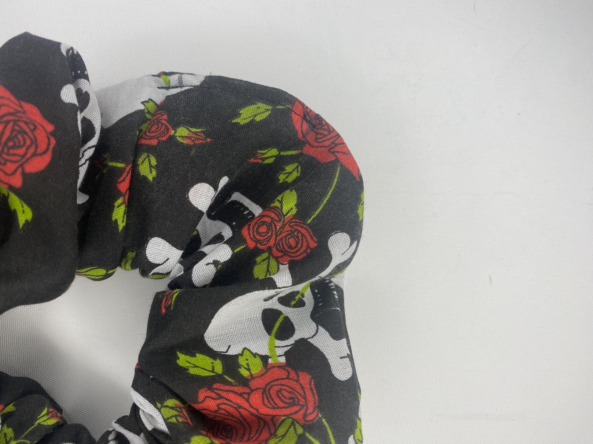 A studio style photo of a large sized scrunchie with skull and crossbones and red roses.