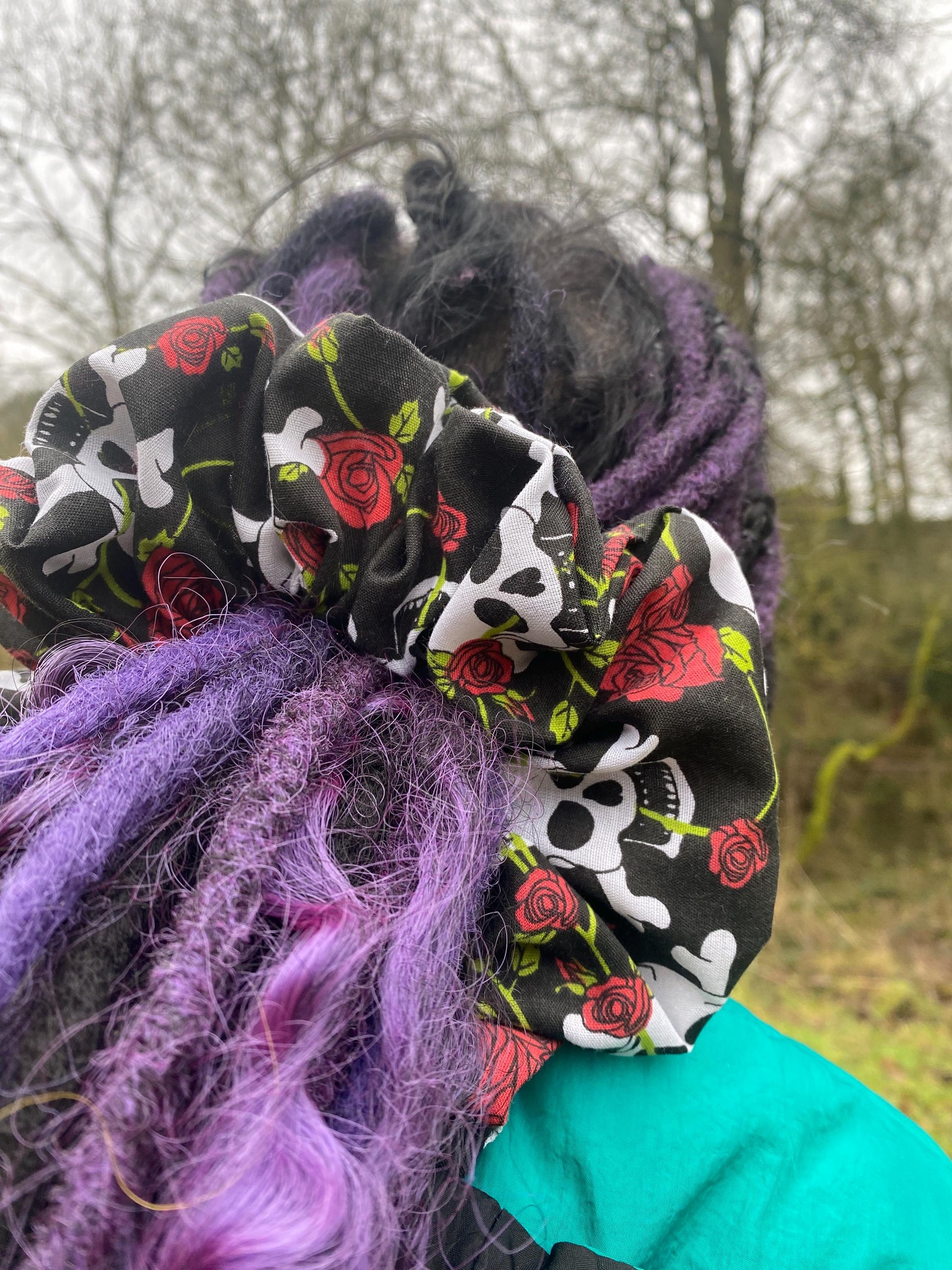 Person sporting purple dreadlocks complemented by a large sized scrunchie with skull and crossbones and red roses.